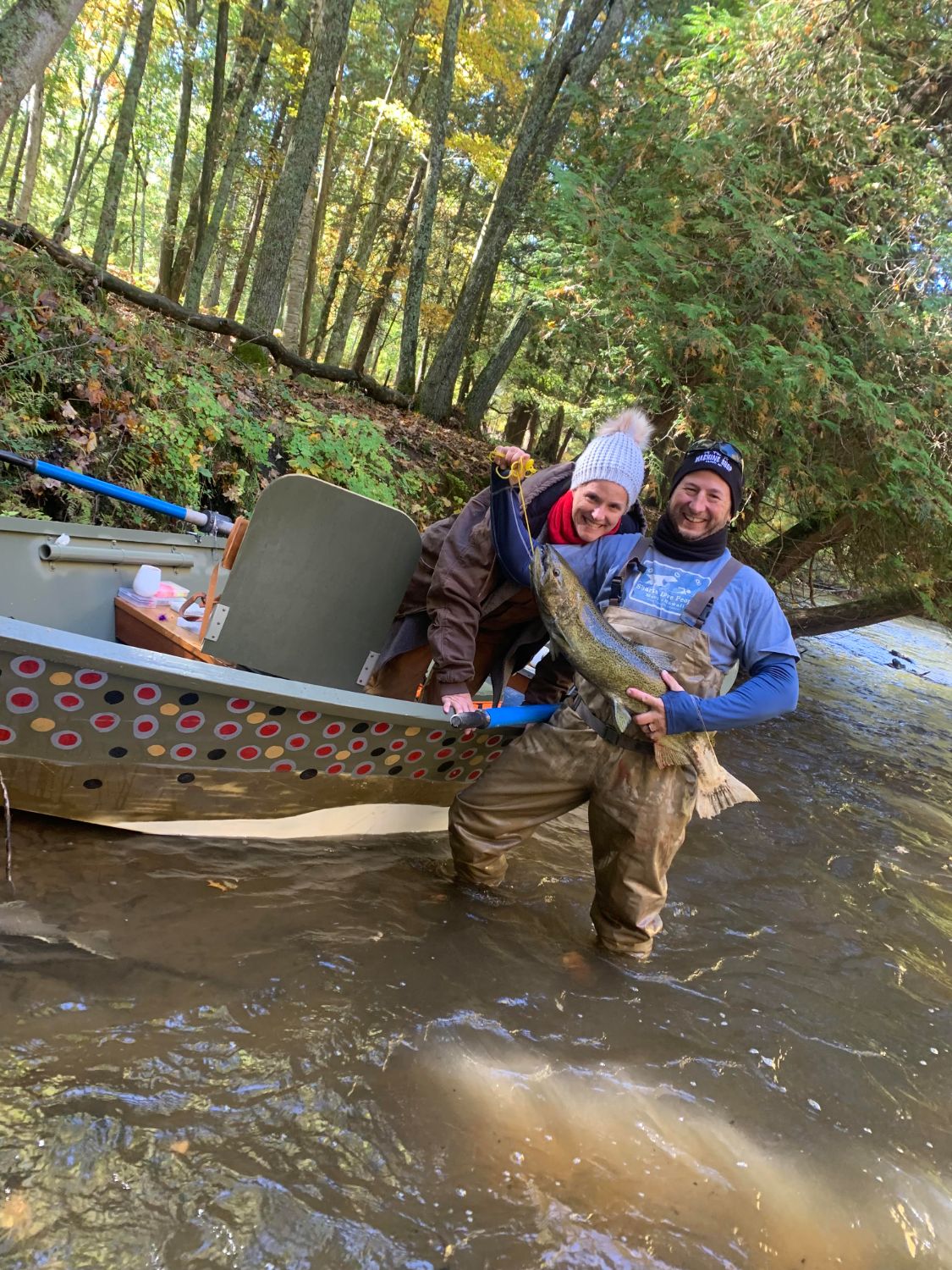 Two anglers smiling with a big salmon beside the painted drift boat